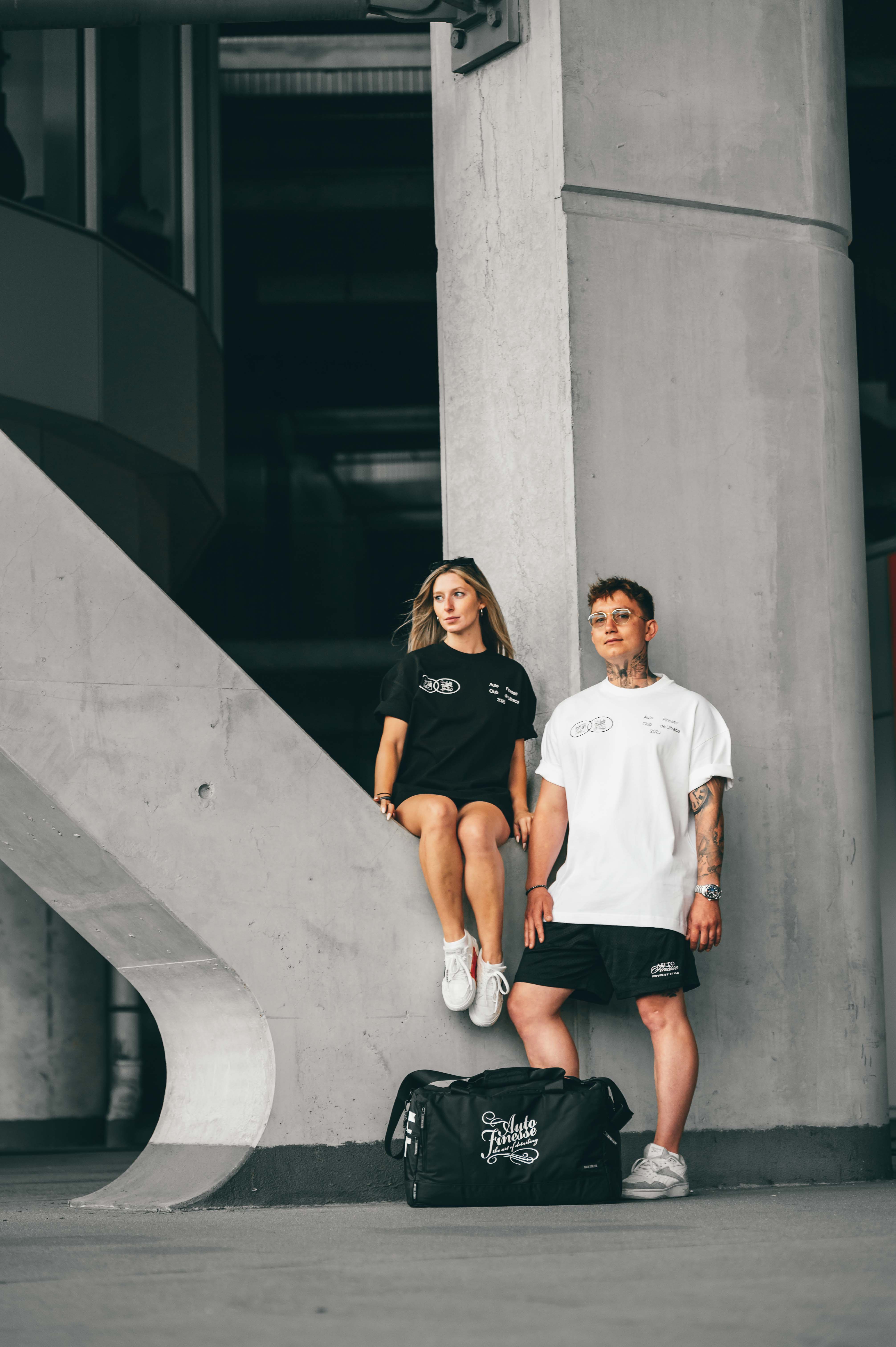 Two people standing next to a black duffel bag in an urban setting.