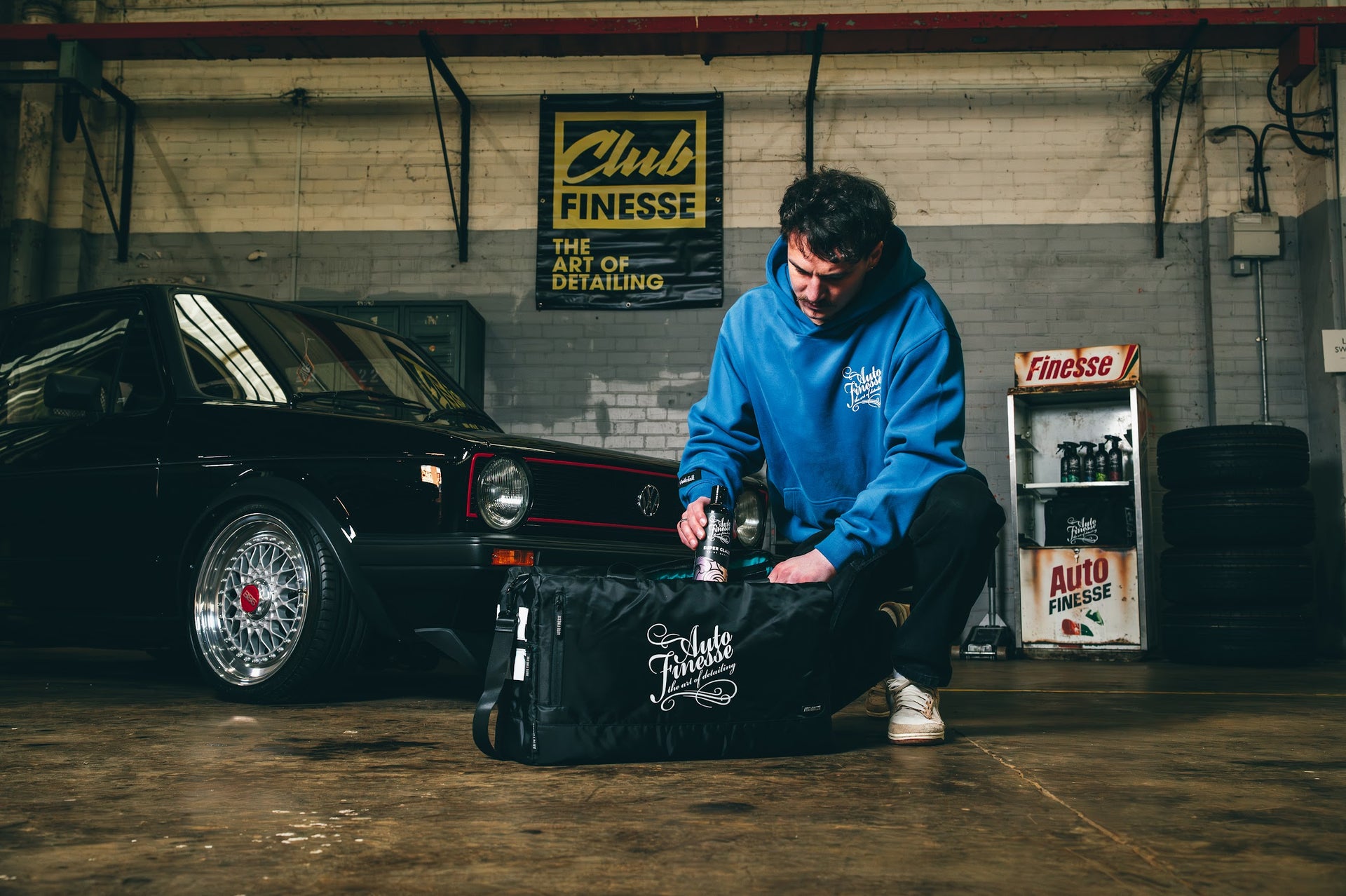 Person in a garage with a car and 'Club Finesse' sign in the background