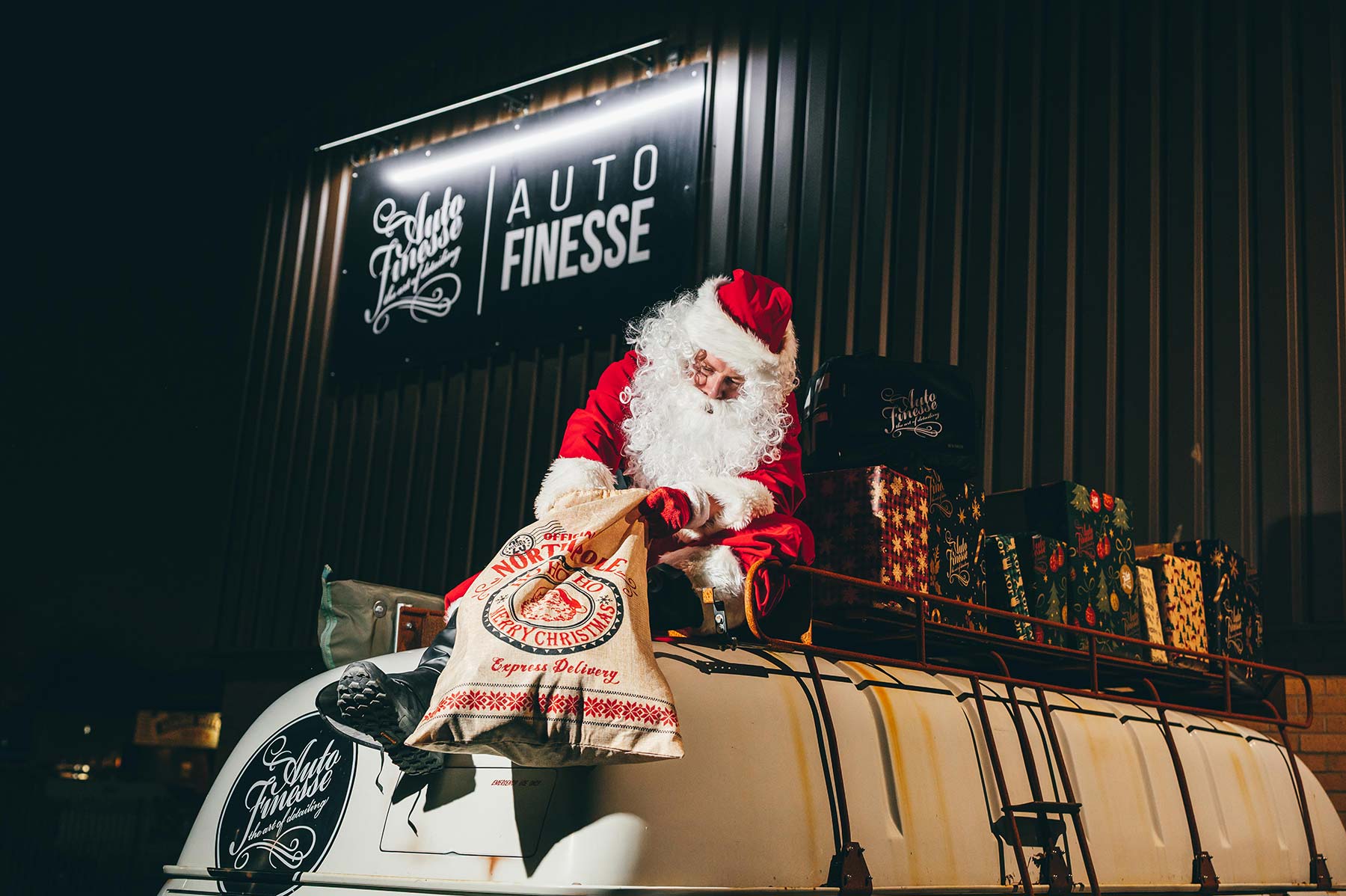 Santa Claus placing Christmas sacks on Auto Finesse van