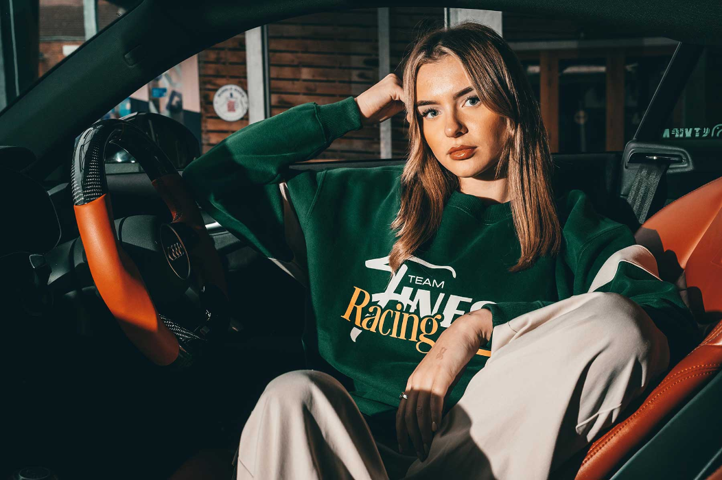 Woman wearing a green sweatshirt with 'Team Fine Racing' text, sitting inside a car.