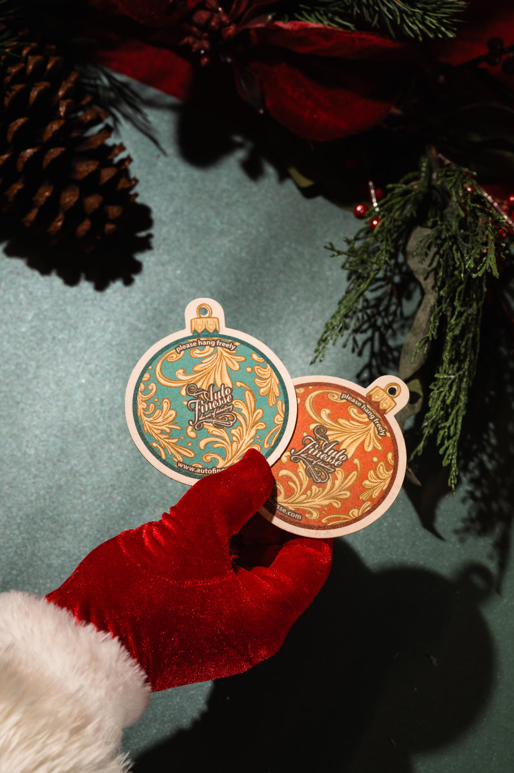 A red-gloved hand holding two Christmas ornament-shaped air fresheners