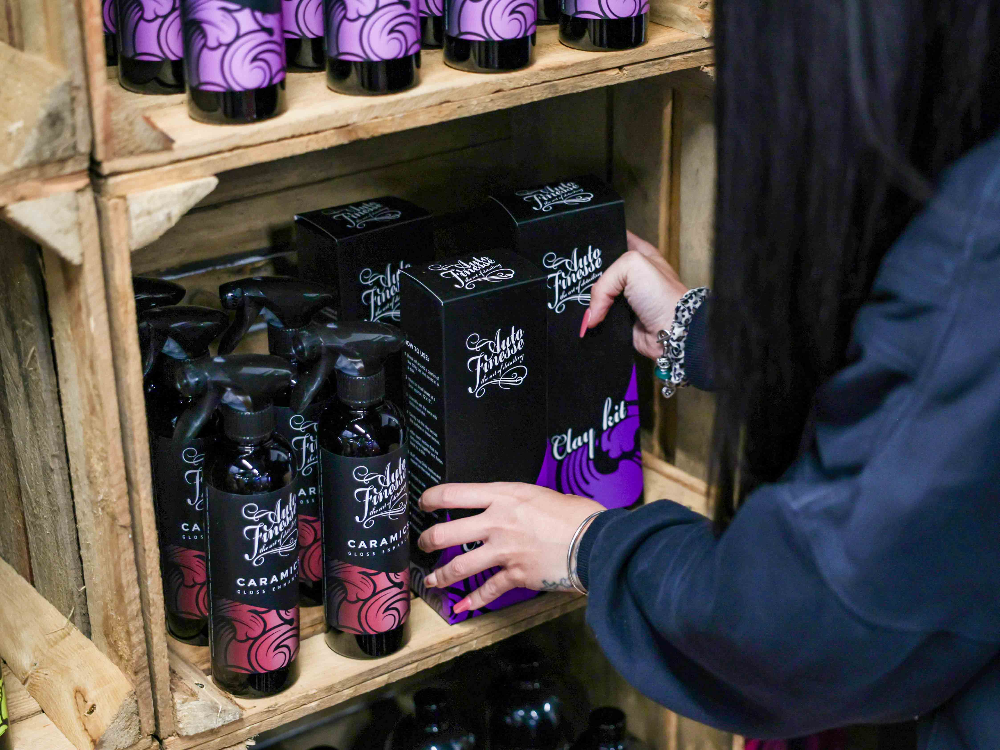 Person selecting a bottle of Fiddle Thistle gin from a wooden shelf with more bottles and boxes.