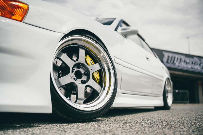 Close-up of a white car's wheel with a visible brand logo on a blurred background