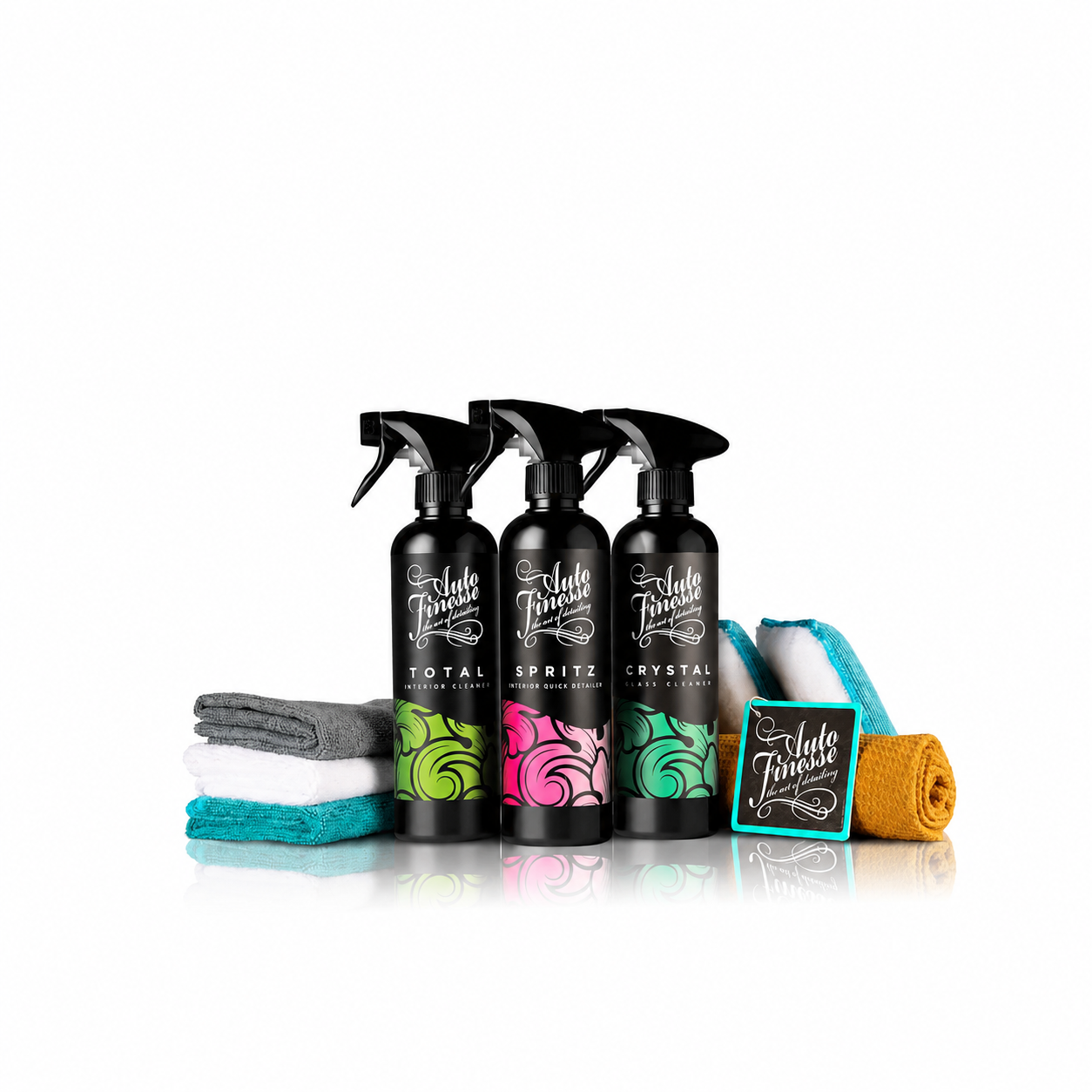 Three black spray bottles labeled 'Turtlefin Total Spritz Crystal' with colorful swirl graphics, displayed with folded and rolled towels in gray, white, teal, turquoise, and orange on a white background.