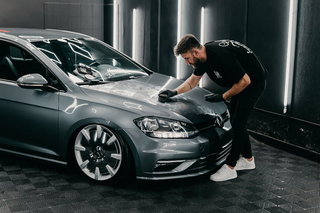 Person cleaning a car with a black vehicle in the background