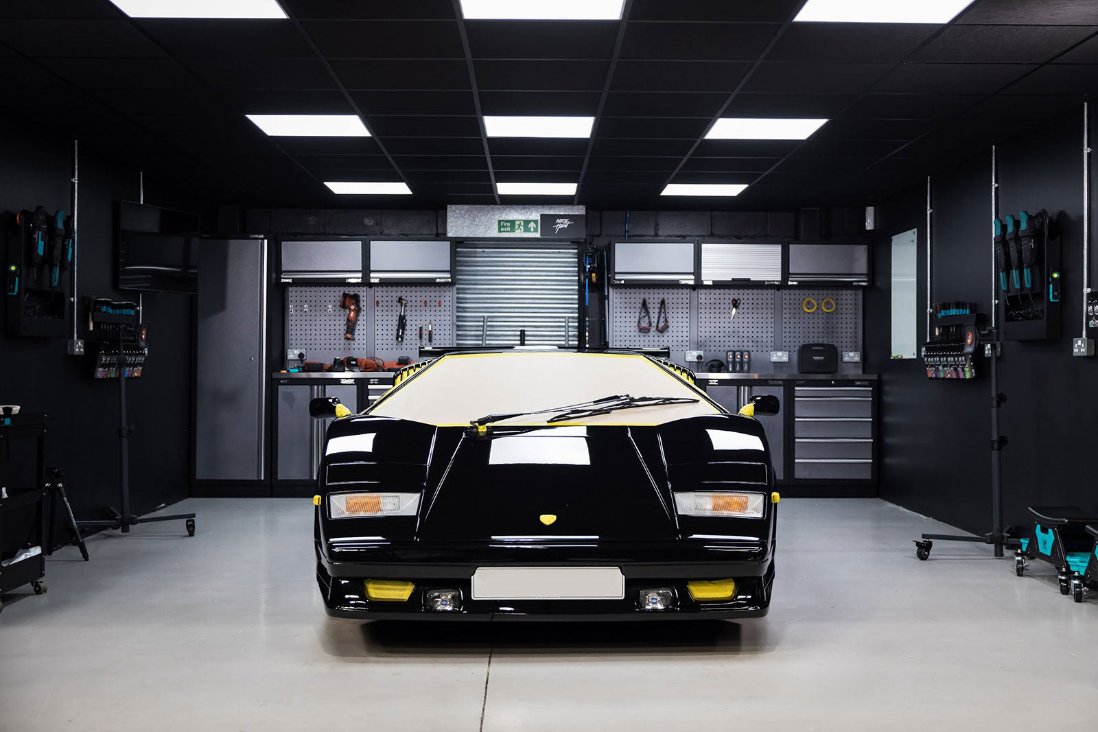 Black sports car in a well-lit garage with tools and equipment.