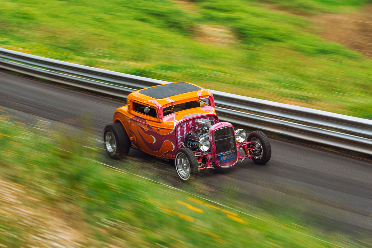 Orange hot rod racing down a green hill track