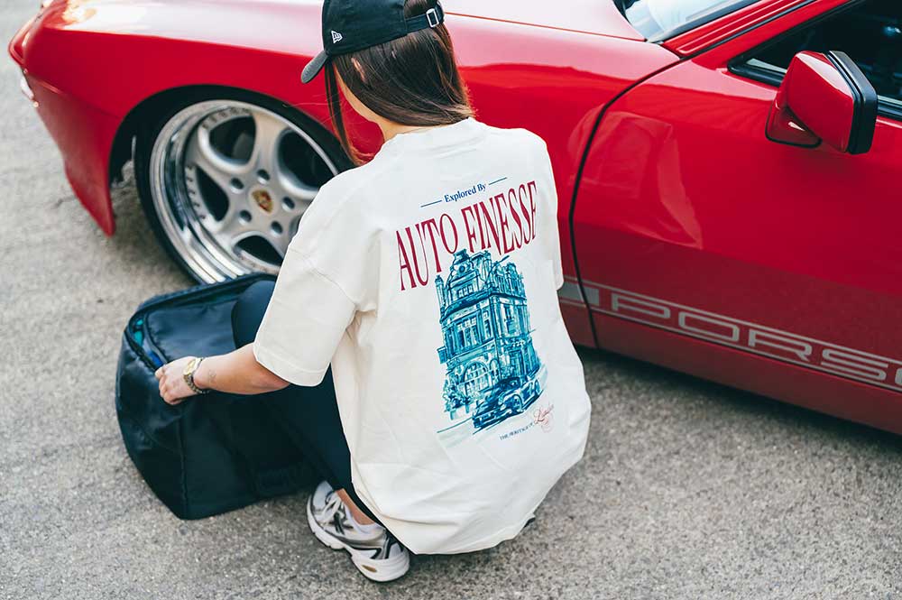 Woman packing bag near red Porsche car wearing Auto Finesse T-shirt