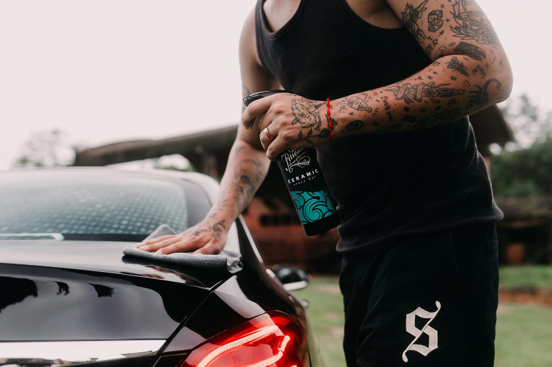 Person holding a bottle of car care product next to a car