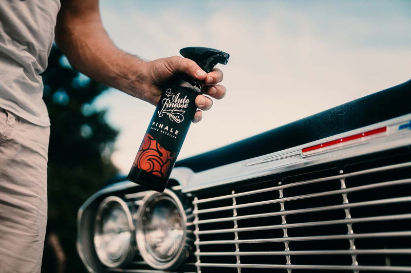 Person holding a spray bottle labeled 'Finals' in front of a car