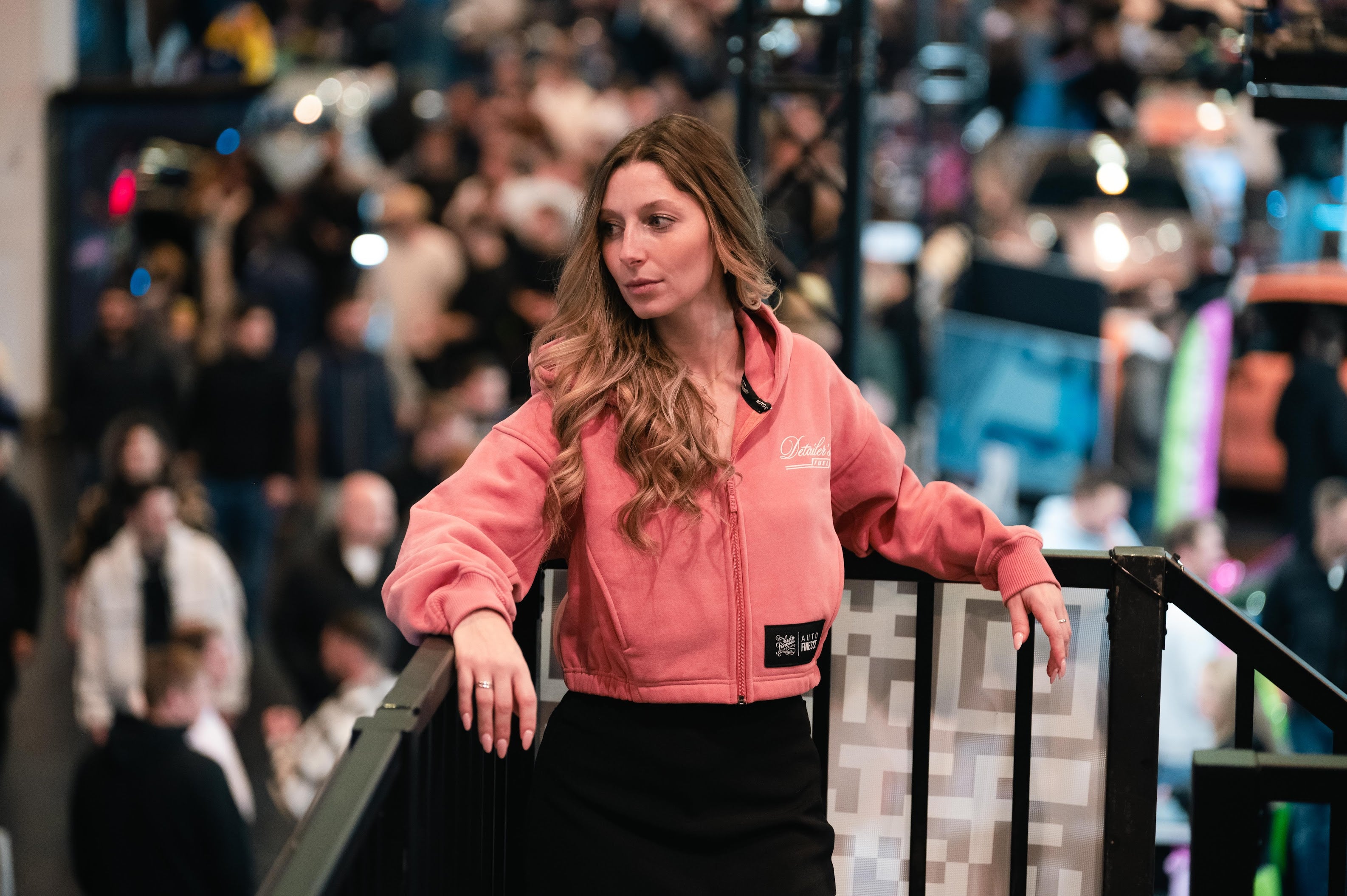Woman leaning on barrier in pink cropped zip Auto Finesse hoodie