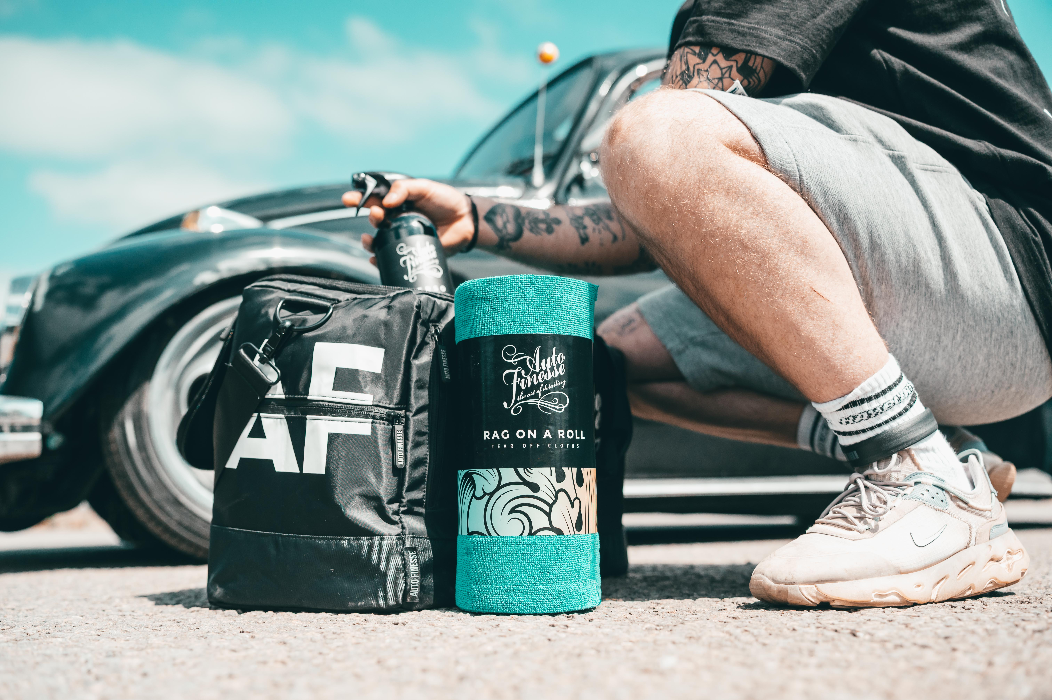 Person sitting on a car with a black bag and teal canister, outdoors.