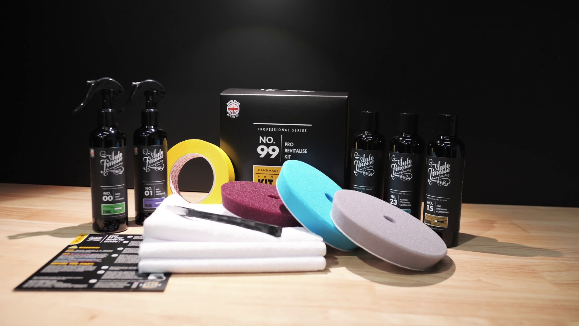 Automotive care products including bottles, cloths, and applicators on a wooden surface with a black background.